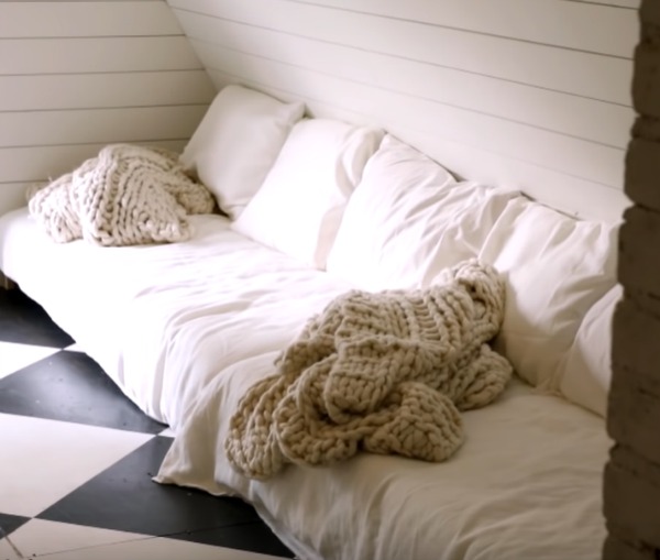 Black and white checkered painted wood floor in an attic with paneled walls and white bedding with cable knit throws. Design by Leanne Ford. #leanneford #whitedecor #blackandwhite #interiordesign