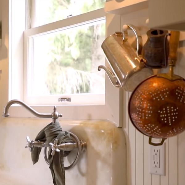 Rustic kitchen with vintage sink with skirt, beadboard, Shaker cabinetry, and pegs for vintage kitchenware. Design by Leanne Ford. #rusticdecor #farmhousekitchen #vintagekitchen #interiordesign #leanneford