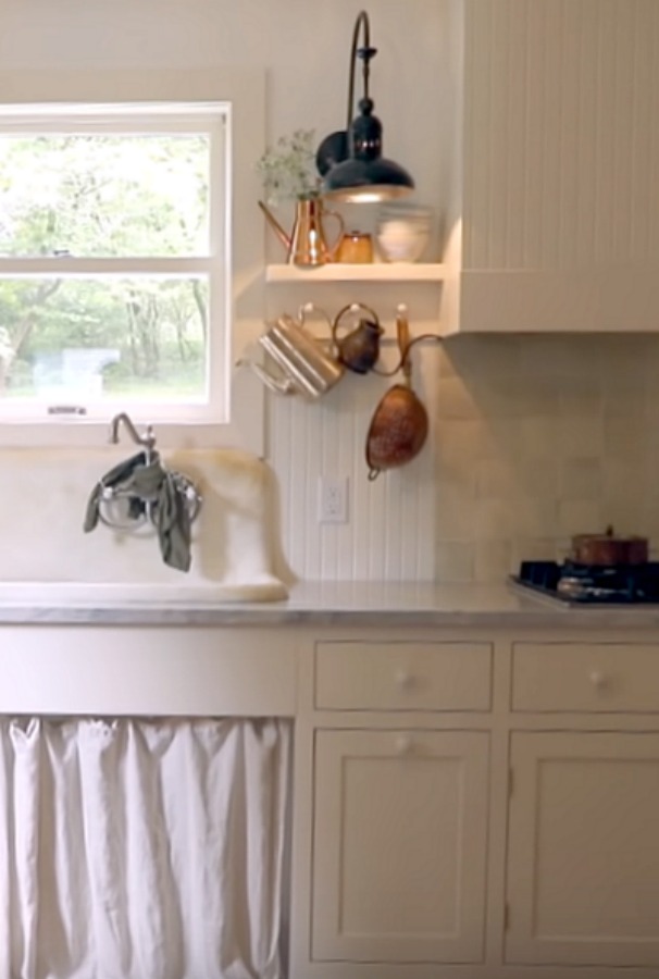 Rustic kitchen with vintage sink with skirt, beadboard, Shaker cabinetry, and pegs for vintage kitchenware. Design by Leanne Ford. #rusticdecor #farmhousekitchen #vintagekitchen #interiordesign #leanneford