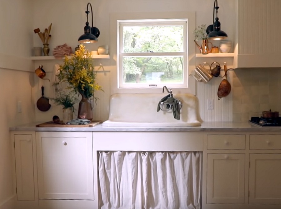 Rustic kitchen with vintage sink with skirt, beadboard, Shaker cabinetry, and pegs for vintage kitchenware. Design by Leanne Ford. #rusticdecor #farmhousekitchen #vintagekitchen #interiordesign #leanneford