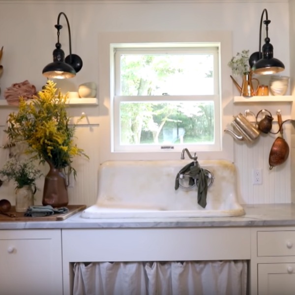 Rustic kitchen with vintage sink with skirt, beadboard, Shaker cabinetry, and pegs for vintage kitchenware. Come steal Leanne Ford's Paint Colors in the Sweetest Country Cottage!. #vintagekitchen #interiordesign #leanneford #ppgsugarsoap #ppgdelicatewhite #paintcolors