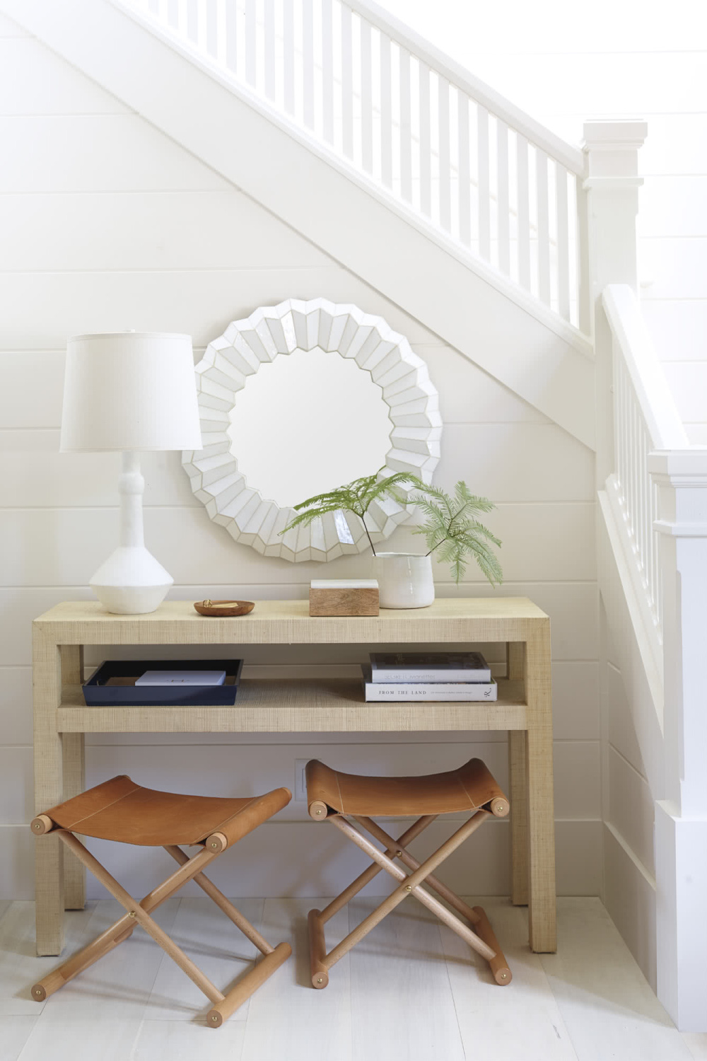 Classic, airy white entry area near staircase in a coastal cottage with Cooper leather stools from Serena & Lily. #leatherstool #foldingstools #coastalfurniture #entry