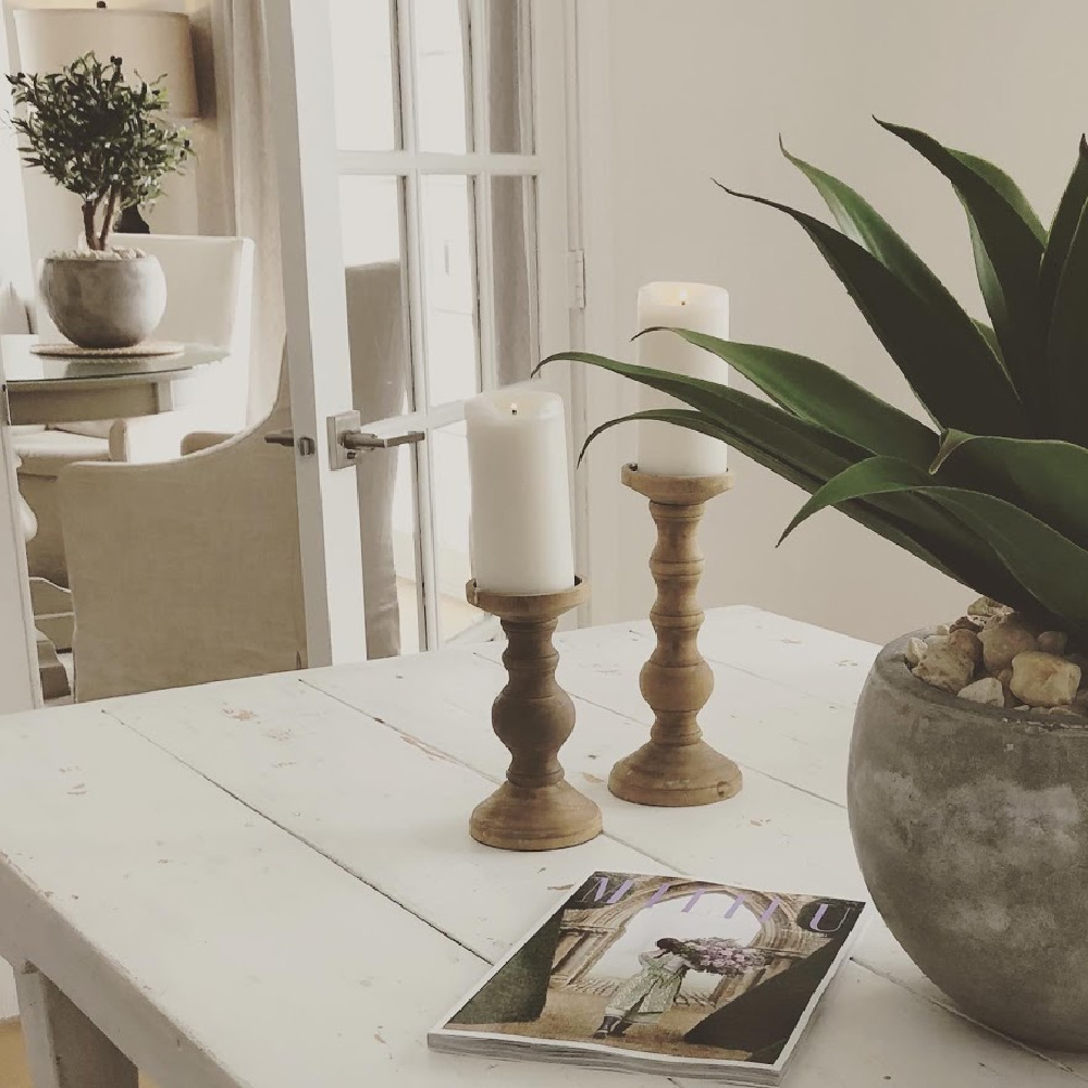 Serene white modern French dining room with farm table, rustic wood candleholders, and succulent in rustic pot - Hello Lovely Studio. #allwhitedecor #modernfrench #diningroom