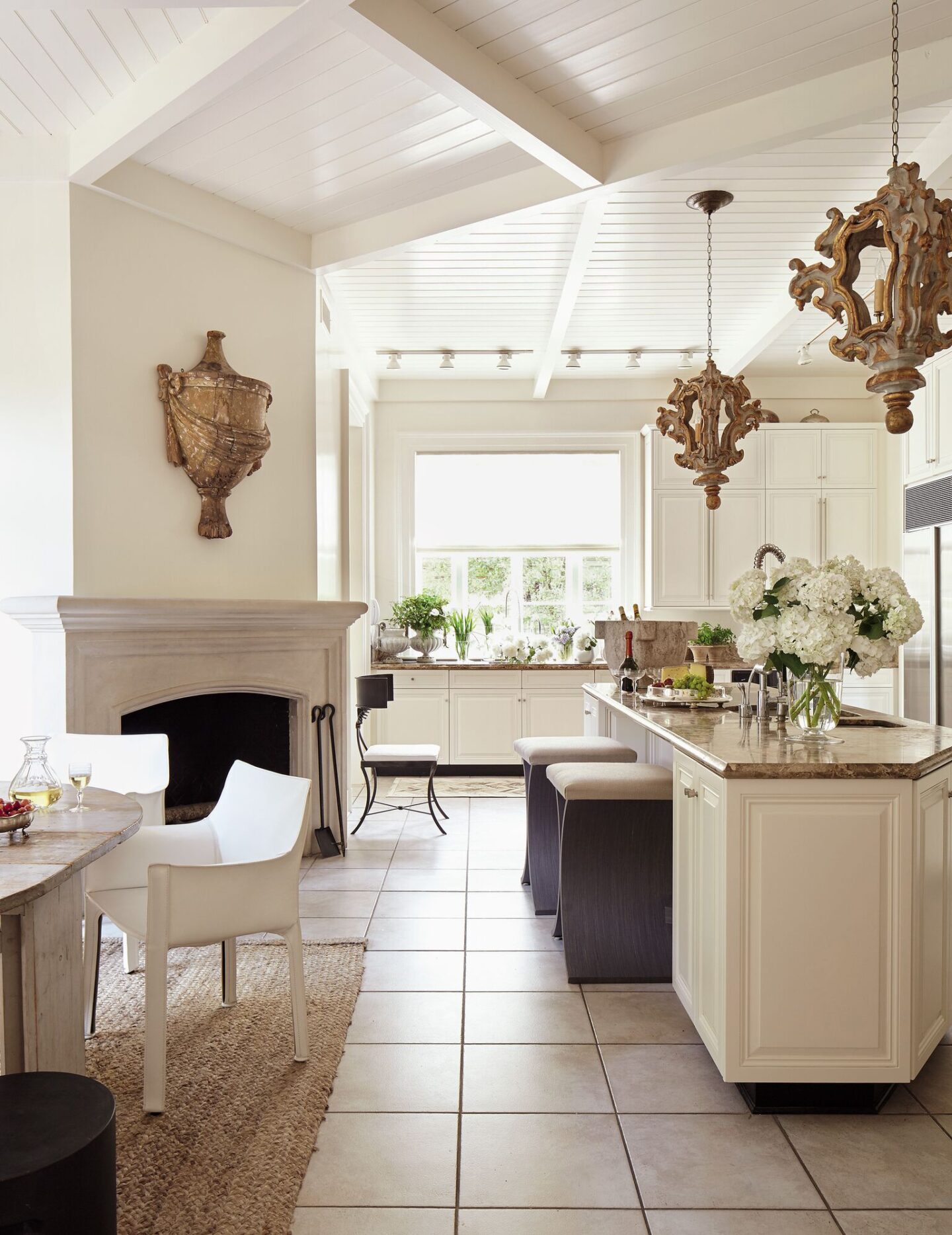 Designer Tara Shaw upgraded a builder's grade kitchen with antiques such as a 19th century urn, 18th century Italian rococo lanterns, and grand stone mortar. #tarashaw #interiordesign #kitchendesign #oldworldstyle #antiques #europeanantiques #whitekitchen #traditionalkitchen #rusticelegance