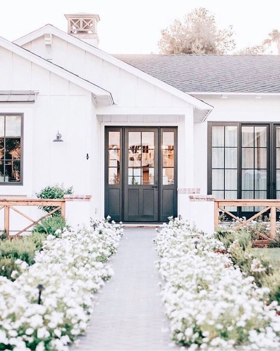 Beautiful white home with black windows and a gorgeous floral flanked path to the front door. Charming inspiration if you love white painted house exteriors! #whitehouses #housedesign #exteriors #curbappeal