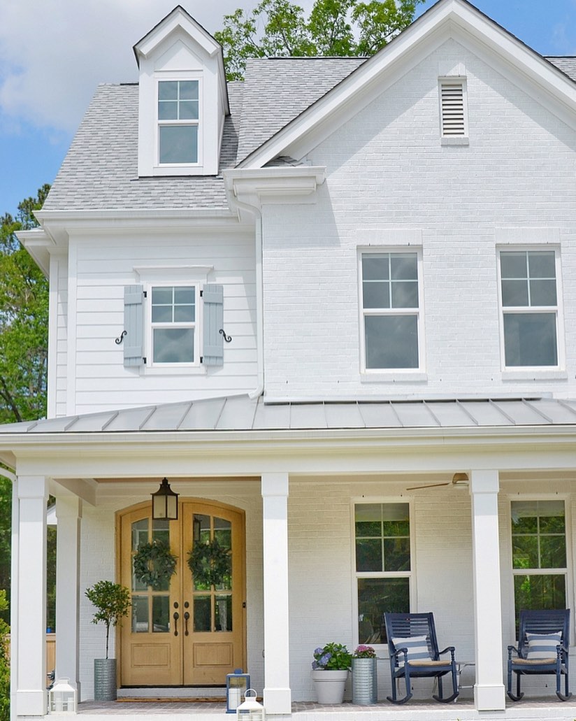 White farmhouse with gorgeous arched double doors and metal roof. Charming inspiration if you love white painted house exteriors! #whitehouses #housedesign #exteriors #whitefarmhouse