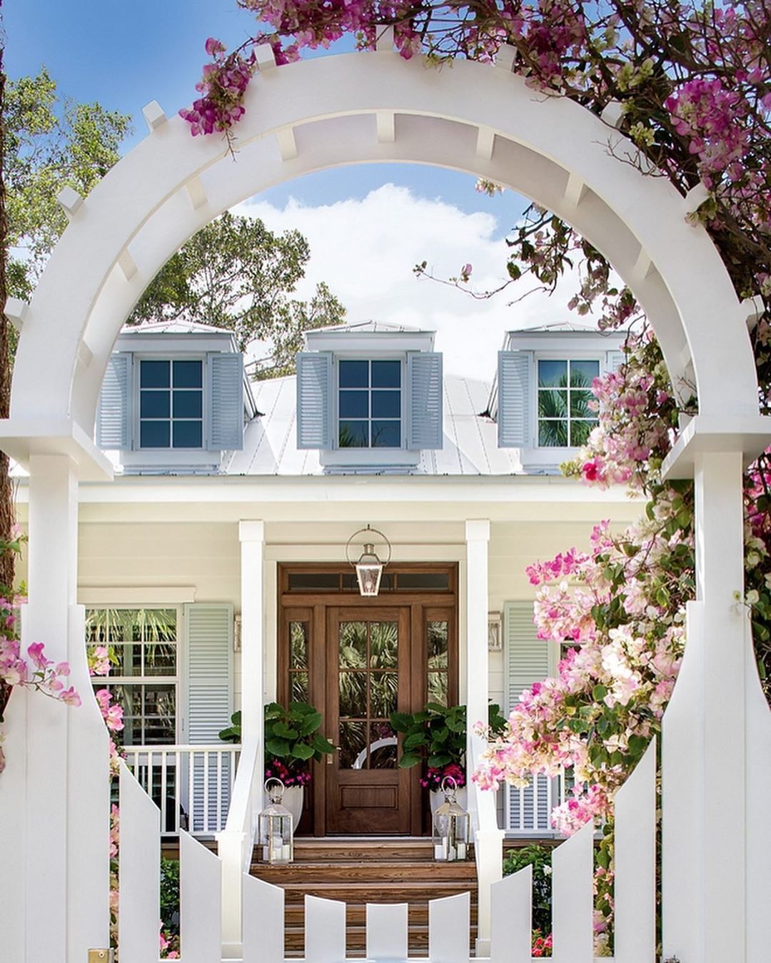 Breathtaking lovely curb appeal with amaazing floral covered arbor and blue shutters - Pineapples Design Group. Peek at Charming Porch Inspiration & Decor Ideas for your home! #whitehouses #housedesign #exteriors #curbappeal #shutters #arbor