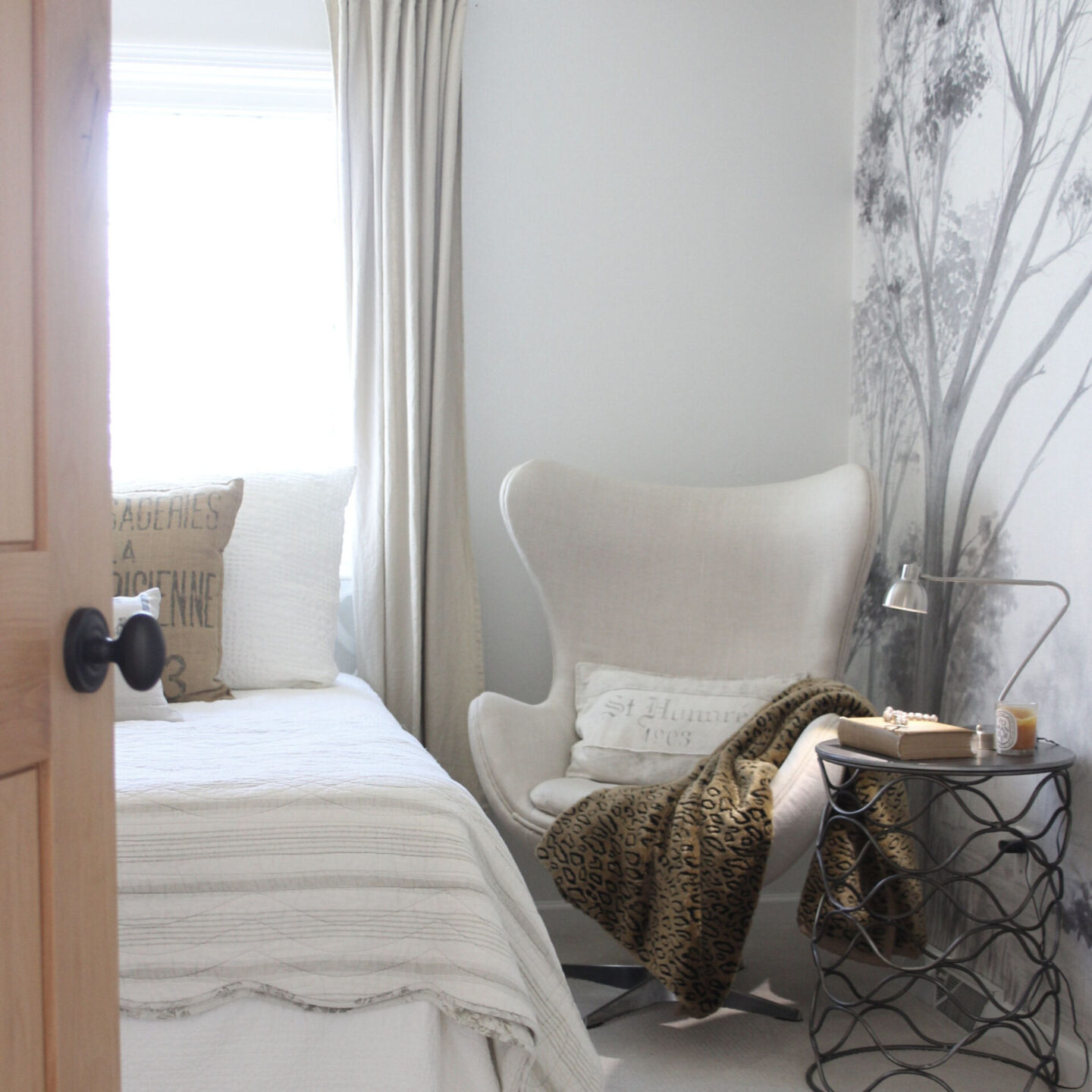 Alder door opens into a neutral bedroom with linen upholstered egg chair and grisaille mural on wall - Hello Lovely Studio. Care to learn how to decorate chic yet cheap?