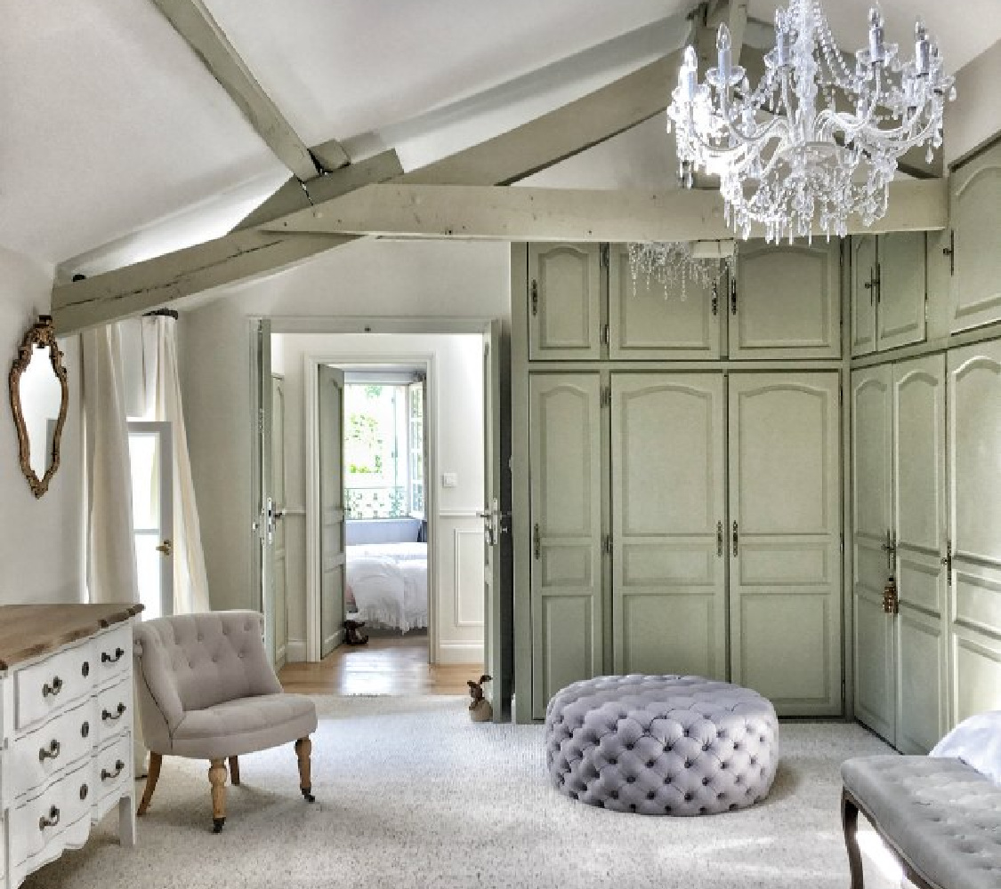 This romantic dressing room in a farmhouse bedroom in France is graced with a luxurious Marie Antoinette style crystal chandelier and built-in cupboards. #frenchfaramhouse #interiordesign #rusticdecor #bedroomdecor #farrowandballstrongwhite #farrowandballfrenchgray