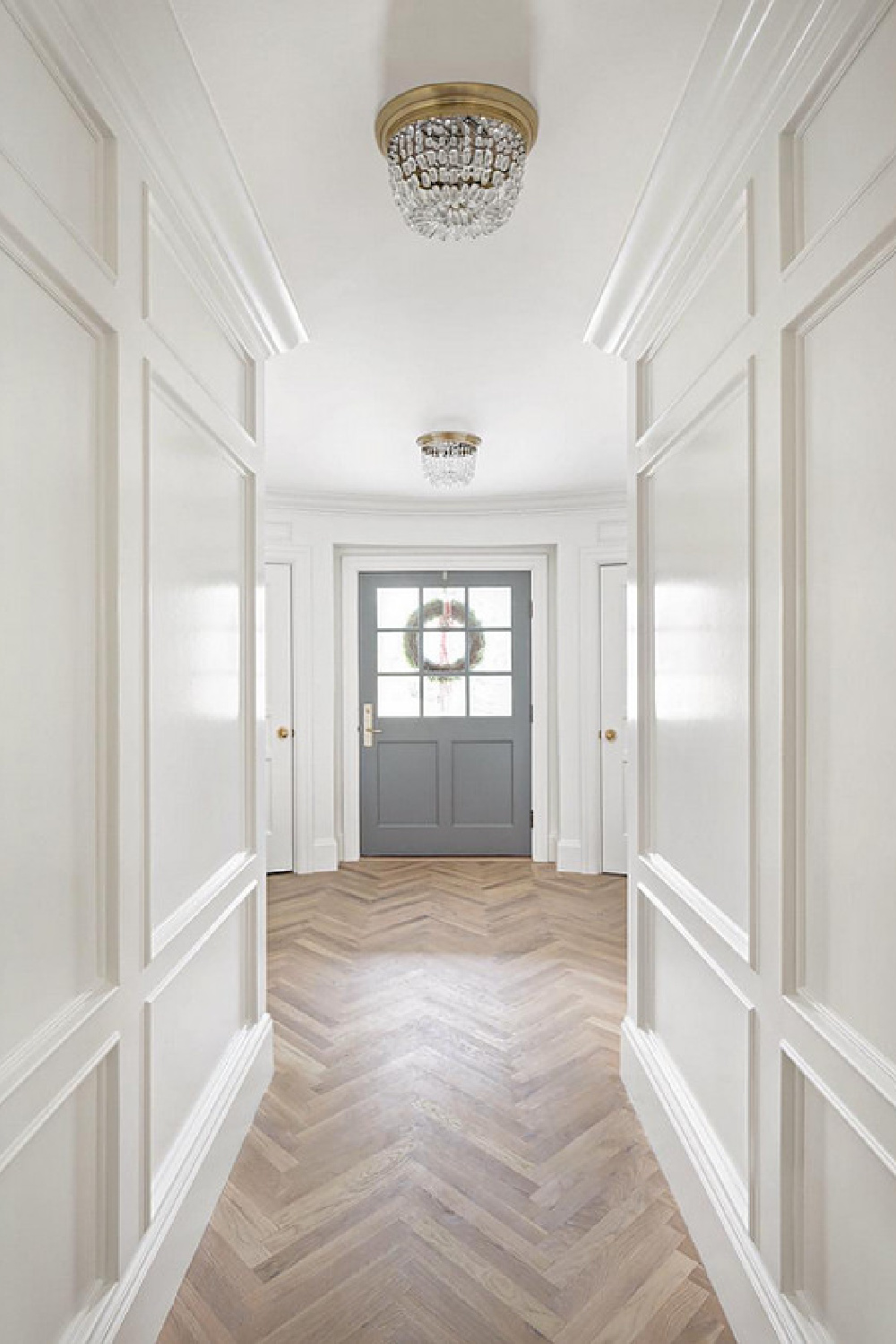 Benjamin Moore Simply White paint color on paneling in a hall. Design by The Fox Group. Herringbone wood floor and beautiful grey painted door. Come BE INSPIRED BY MORE Timeless Interior Design Ideas, Paint Colors & Furniture Finds. #thefoxgroup #benjaminmooresimlywhite #herringbone #woodfloor #interiordesigninspiration