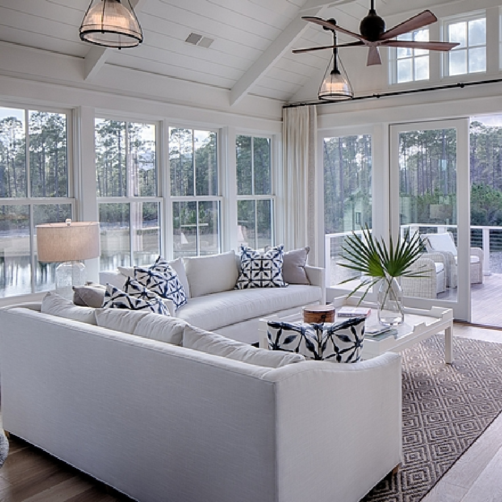 Great room with white oak flooring, white sofas, blue accessories, and shiplap in a board and batten coastal cottage in Palmetto Bluff. Modern farmhouse interior design by Lisa Furey. #greatroom #coastalstyle #blueandwhite #whiteoak #shiplap #breezystyle #interiordesign