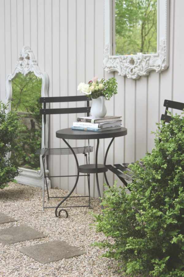 French country style courtyard with pea gravel and black metal modern French bistro dining area and boxwood. #hellolovelystudio #cafechairs #outdoordining #patiofurniture #modernfrench #courtyard #outdoorfurniture