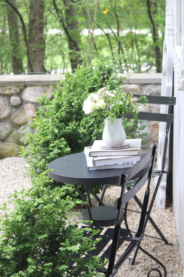 French country style courtyard with gravel and stonewall with a black modern French bistro dining area and boxwood. #hellolovelystudio #frenchcountry #modernfrench #courtyard #graden #outdoordining #outdooroasis