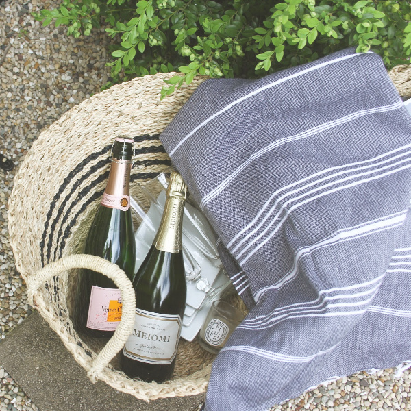 Fancy Parisian style picnic essentials in a black stripe French seagrass basket with Turkish throw. #hellolovelystudio #parisianstyle #frenchcountry #champagne #turkishthrow #frenchpicnic #milieumoment