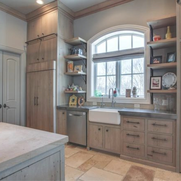 Kelly Clarkson's beautiful farmhouse kitchen in her Tennessee mansion has a farm sink wall with arched window and open shelving. #farmhousekitchen #farmsink #kitchendesign #kellyclarkson #frenchfarmhouse