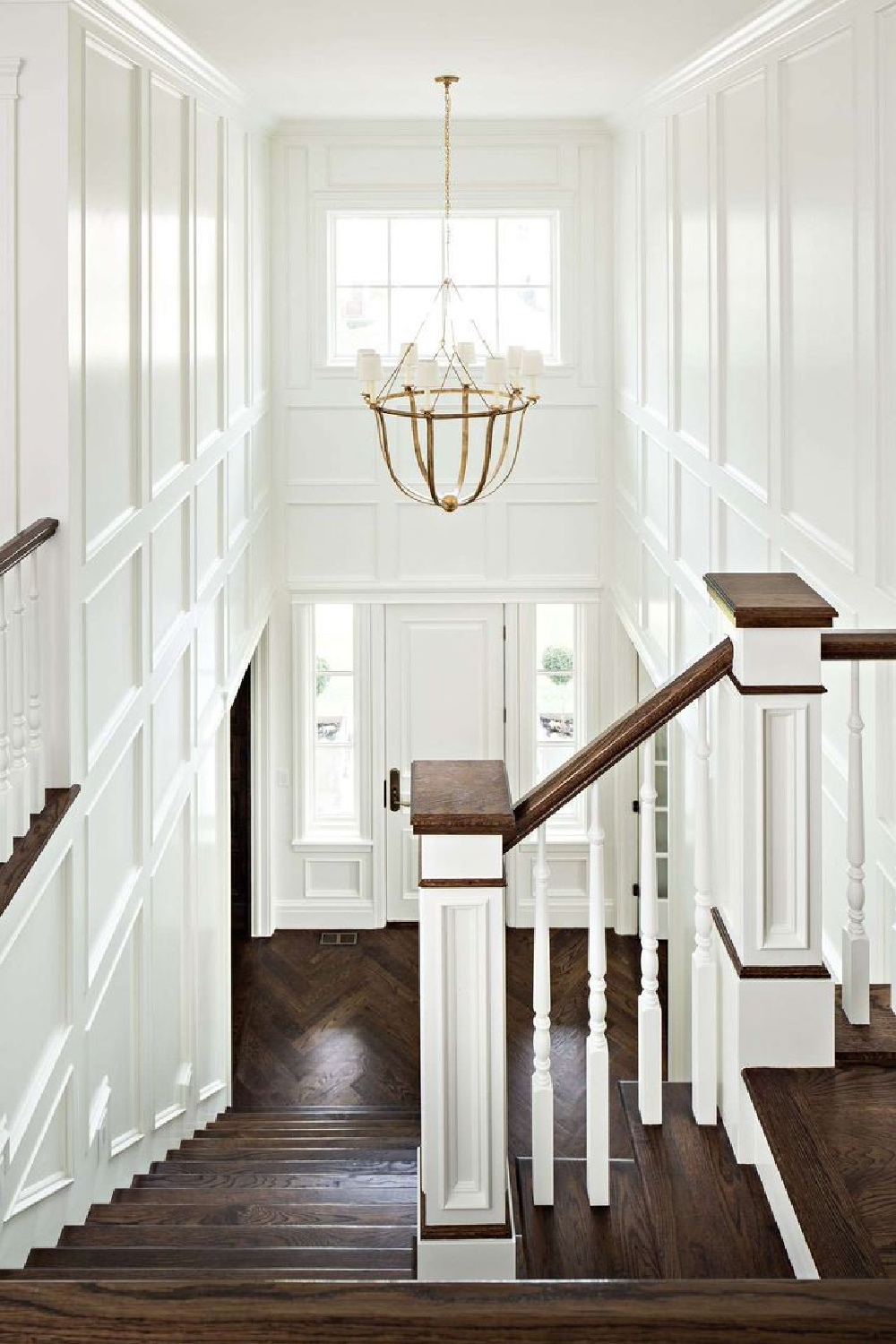 Richly stained dark hardwood flooring and crisp white formal white painted wood paneling in a magnificent entry and staircase. Design by The Fox Group. #staircase #entry #paneling #thefoxgroup