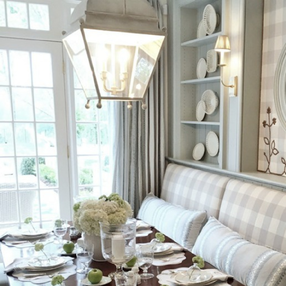 Breakfast dining area in an Atlanta showhouse kitchen has traditional antiques, built-in banquette upholstered in light blue Buffalo check, and bespoke upholstery and drapes. Lauren DeLoach. #diningroom #traditionalstyle #interiordesign #lightblue