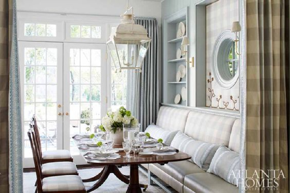 Light blue Buffalo check upholstery, built-in shelves with antique creamware, and custom banquette with round window in a magnificent traditional dining room - Lauren DeLoach is designer.