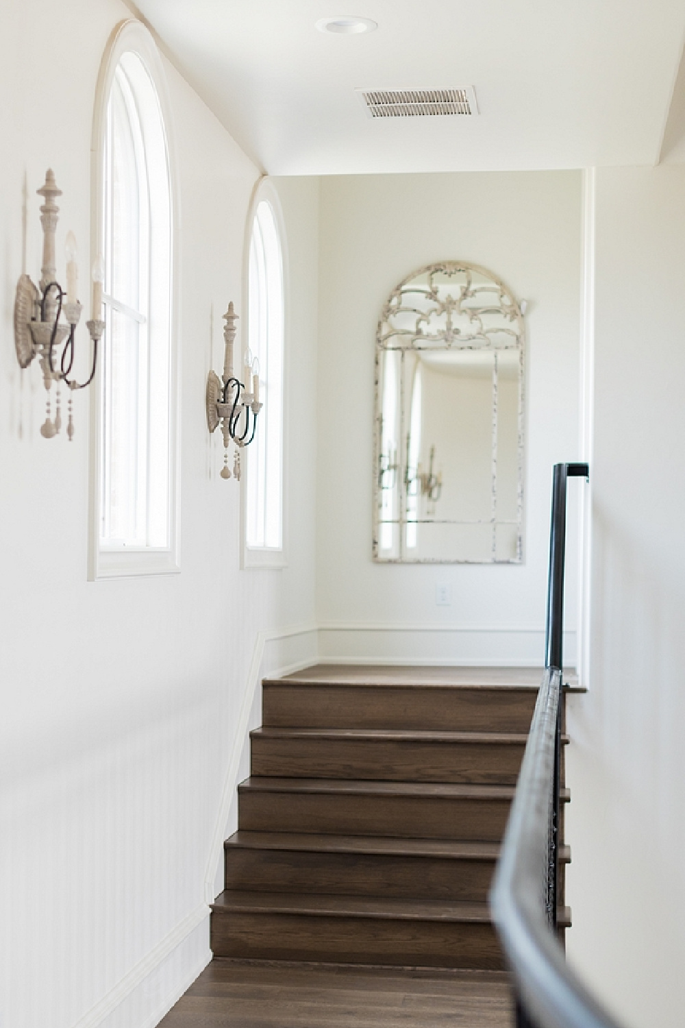 French country sconces and arched mirror in a stairway - Brit Jones.