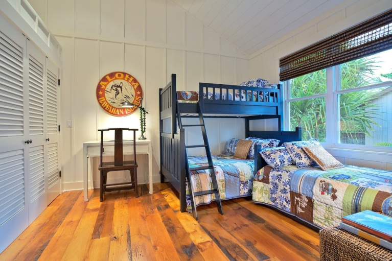 Reclaimed barnwood flooring adds rusticity in a cheerful bunk room with navy beds and a Hawaiian theme. #wideplankflooring #carlisle #hardwoodfloor #interiordesign #reclaimed #barnwood #bunkroom