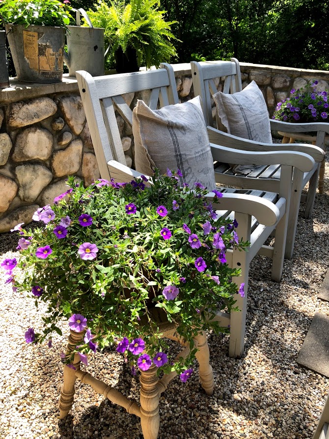 Pretty purple annuals perched on a rustic wood stool in my French country courtyard with pea gravel. #hellolovelystudio #frenchcountry #courtyard #summergarden #rusticstool