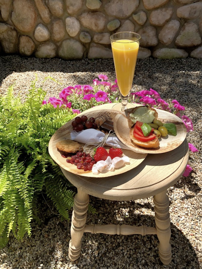 Sweet and savory nibbles and mimosa served on a rustic stool doubling as a cocktail table in the garden - Hello Lovely Studio. #hellolovelystudio #outdoorentertaining #summerentertaining #appetizers #rusticstool #gardenparty