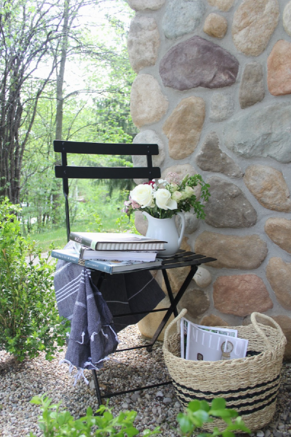 French bistro chair and stripe Turkish throw tucked in a corner of my garden to invite relaxation and reading (cookbooks are my idea of relaxation!). #hellolovelystudio #frenchcountry #bistrochair #turkishthrow #seagrassbasket #turkishtowel #outdooroasis #romanticgarden #outdoordecor #bistrochairs