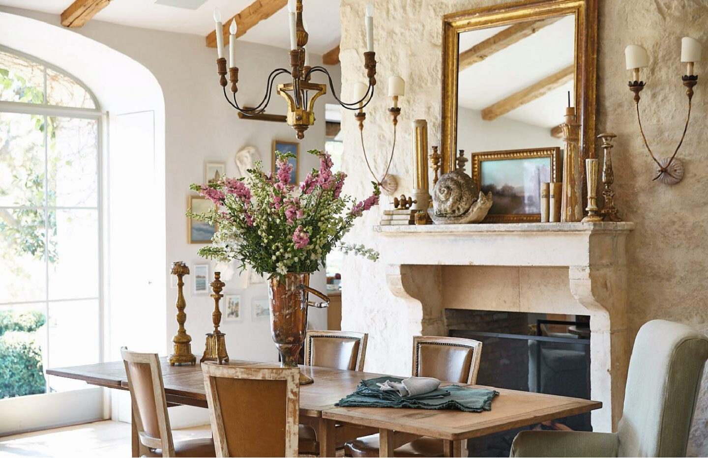 Patina Living photo of dining room with limestone French mantel, French farmhouse chandeliers, plaster walls, and rustic modern farmhouse style. Brooke Giannetti and Steve Giannetti designed the space at Patina Farm. Photo by Victoria Pearson. #patinafarm #limestonefireplace #frenchfarmhouse #interiordesign #modernfarmhouse #diningrooms