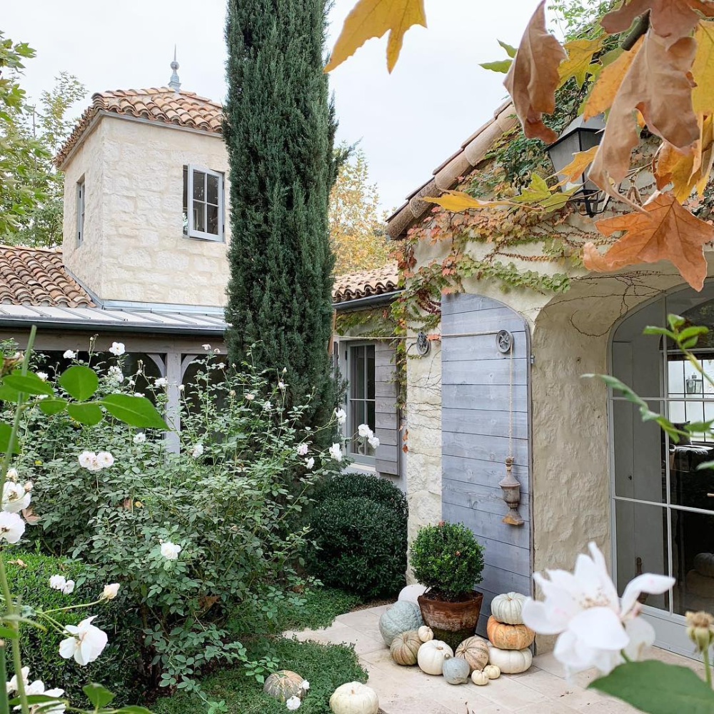Patina Farm exterior in fall with rustic shutters, rugged stone, and lush gardens. Brooke Giannetti. #patinafarm #exterior #stonefarmhouse #modernfarmhouse #frenchfarmhouse #fallgarden #ojaicalifornia #giannettihome