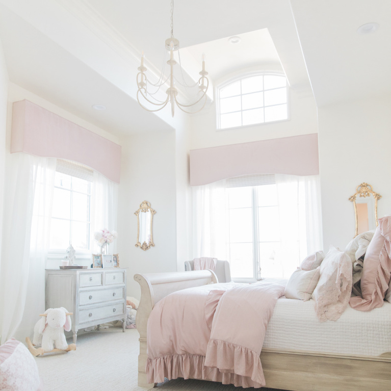 Blush pink girls bedroom with French country style and soaring ceiling with chandelier - Brit Jones Design. See more romantic pastel paint colors and ideas to get this look! #bedroomdecor #girlsbedroom #interiordesign #romanticdecor #pinkbedrooms #paintcolors #sherwinwilliamsalabaster