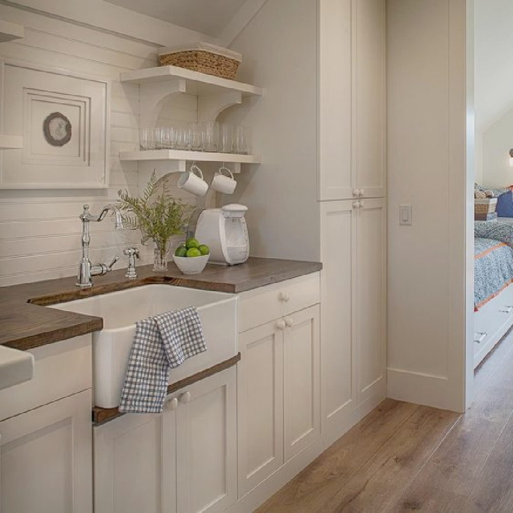 Coastal style kitchenette with custom Shaker cabinetry, farm sink, and open shelving in a charming carriage house by Lisa Furey. Explore more Coastal Cottage Inspo, Paint Colors & Whimsy Quotes Now!