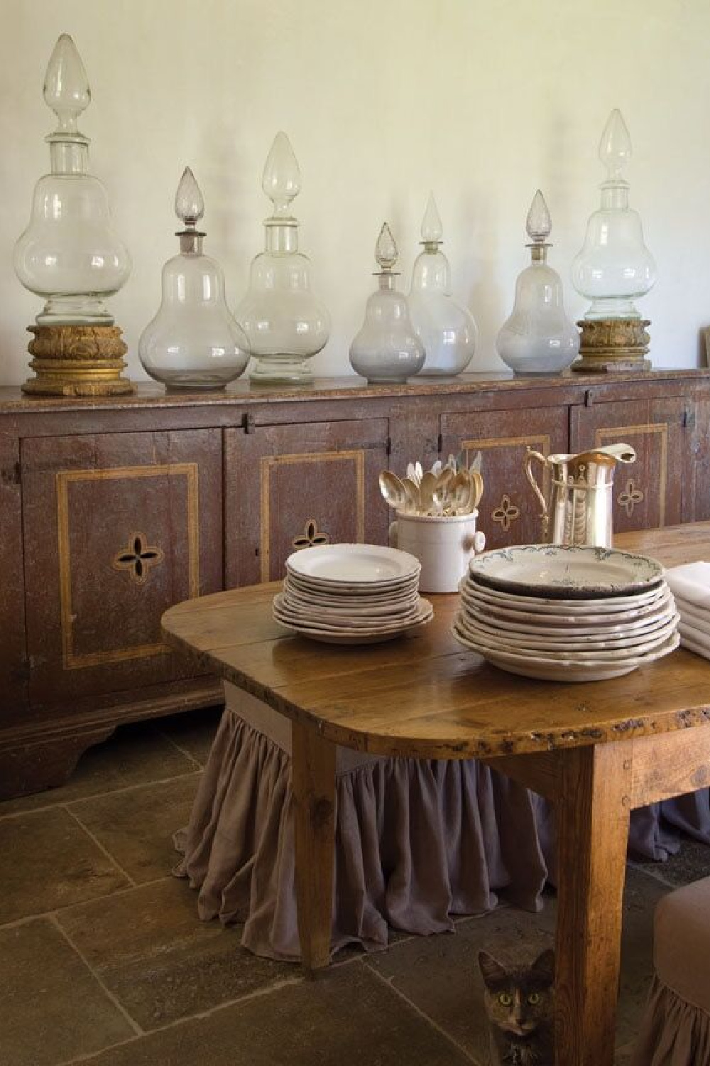 Antique French farmhouse table, sideboard, and collected European country treasures in Ruth Gay's dining room. Chateau Domingue Timeless European Elegance and French farmhouse style converge in this house tour of founder Ruth Gay's home on Hello Lovely. Reclaimed stone, antique doors and mantels, and one of a kind architectural elements. #housetour #frenchcountry #frenchfarmhouse #europeanfarmhouse #chateaudomingue #rusticdecor #pamelapierce #elegantdecor #apothecaryjars #diningroom