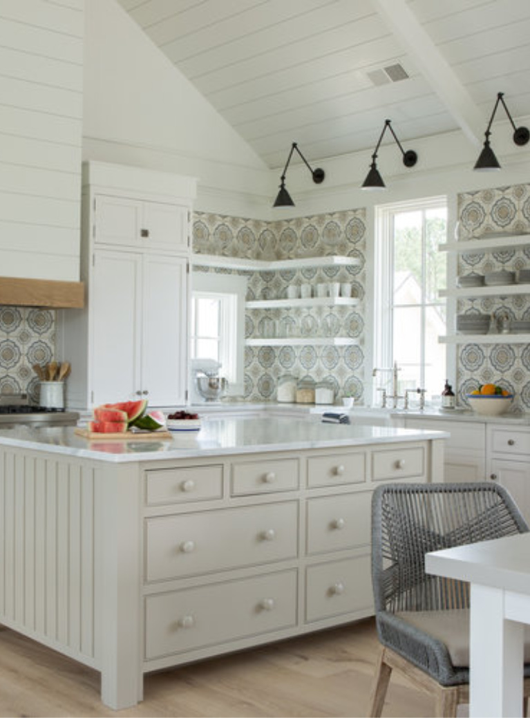 White coastal cottage kitchen with floating shelves, Shaker cabinets, white oak, and cement tile backsplash with blue accents. Lisa Furey. #coastalkitchen #whitekitchens #kitchendesign #modernfarmhouse #coastalcottage #cottagekitchen #floatingshelves #farmsink #shiplap