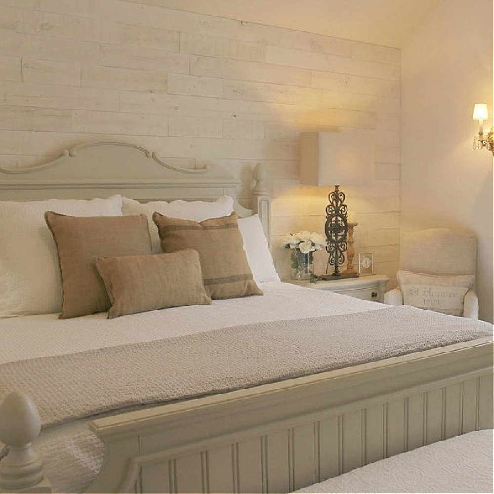 Pale neutral Country French bedroom with Stikwood Hamptons accent wall, beadboard panel bed, and burlap throw pillows on white linens - Hello Lovely Studio.