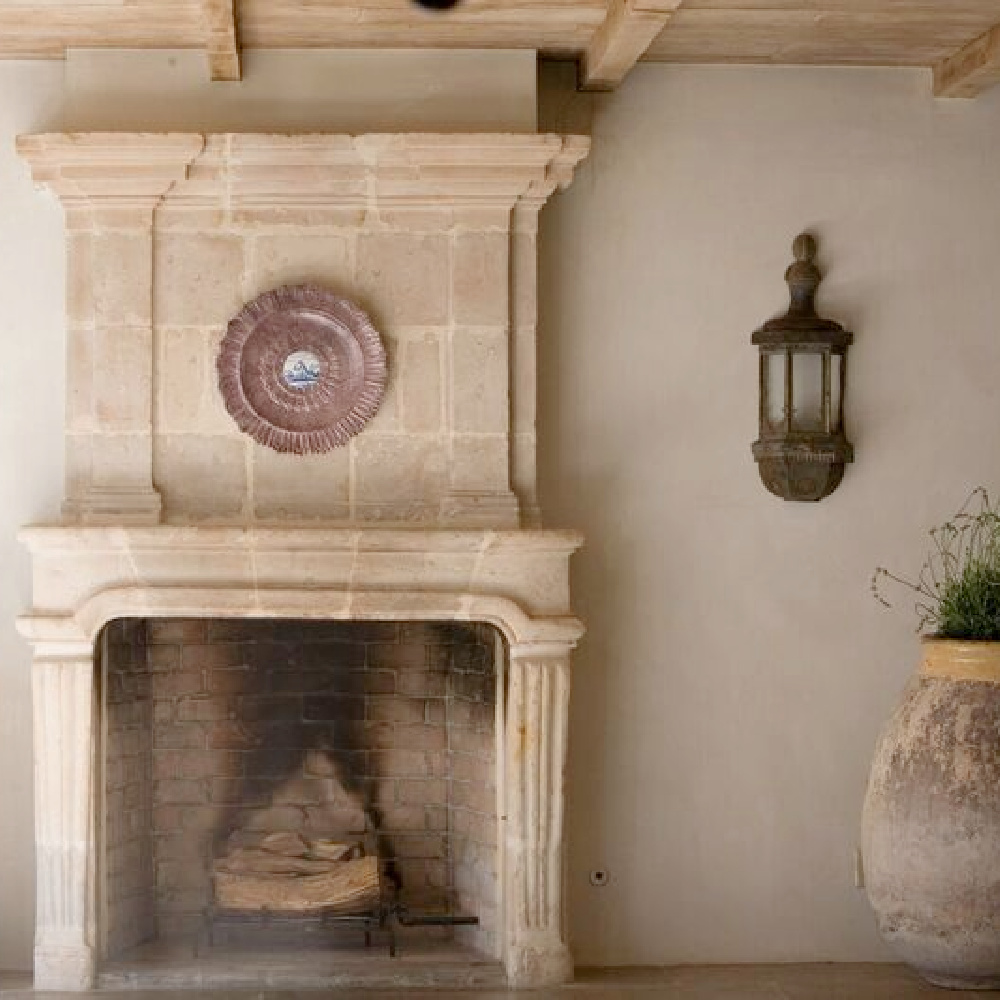 Chateau Domingue antique limestone fireplace with fluted detail, French confit pot, and reclaimed lantern in a serene interior within Ruth Gay's breathtaking Houston home. #oldworld #limestonefireplace #frenchfireplace #antiquefireplacesurround