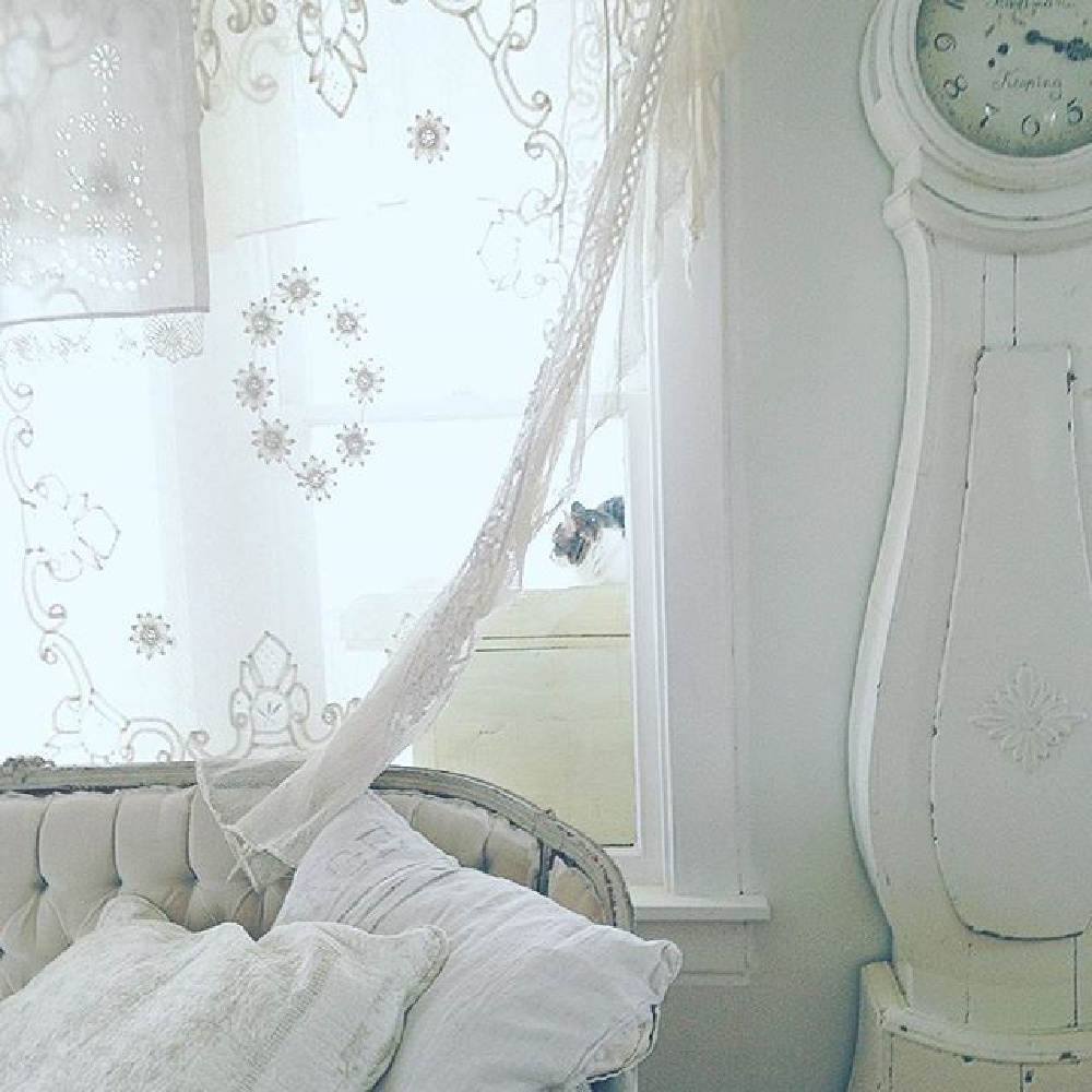 White Swedish Mora clock and tufted velvet settee in a cottage living room with serene vibe by My Petite Maison.