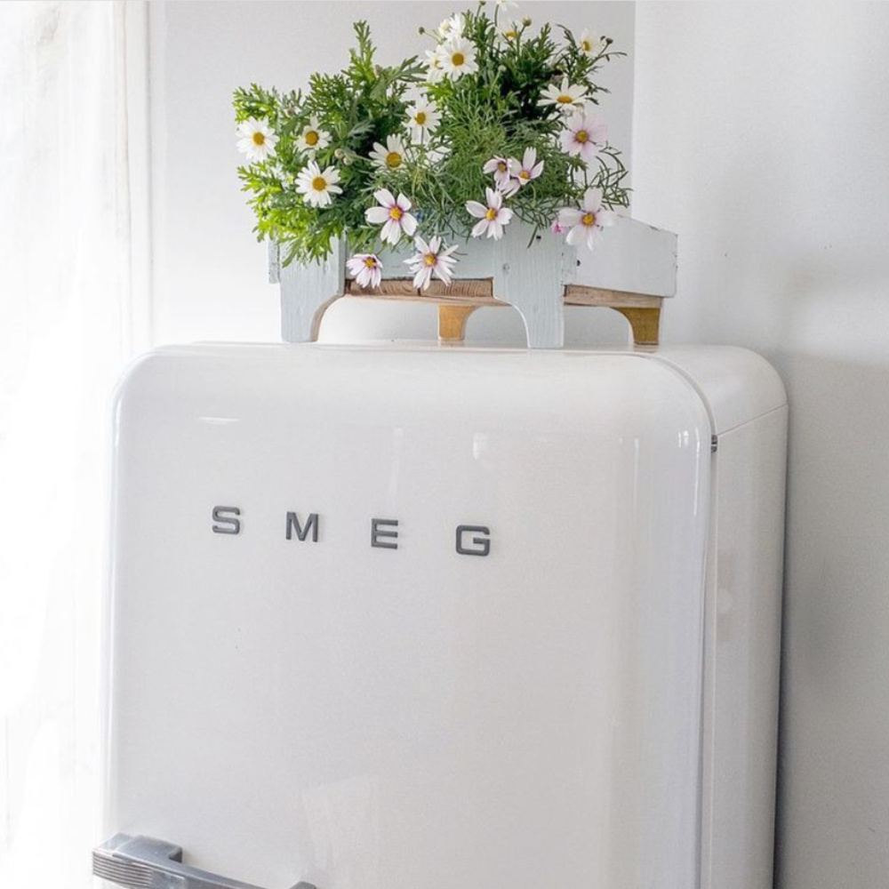 Adorable white Smeg refrigerator with daisies displayed in an old Swedish blue painted crate - @mypetitemaison. #frenchnordic #nordicfrench #frenchkitchen #vintagekitchen