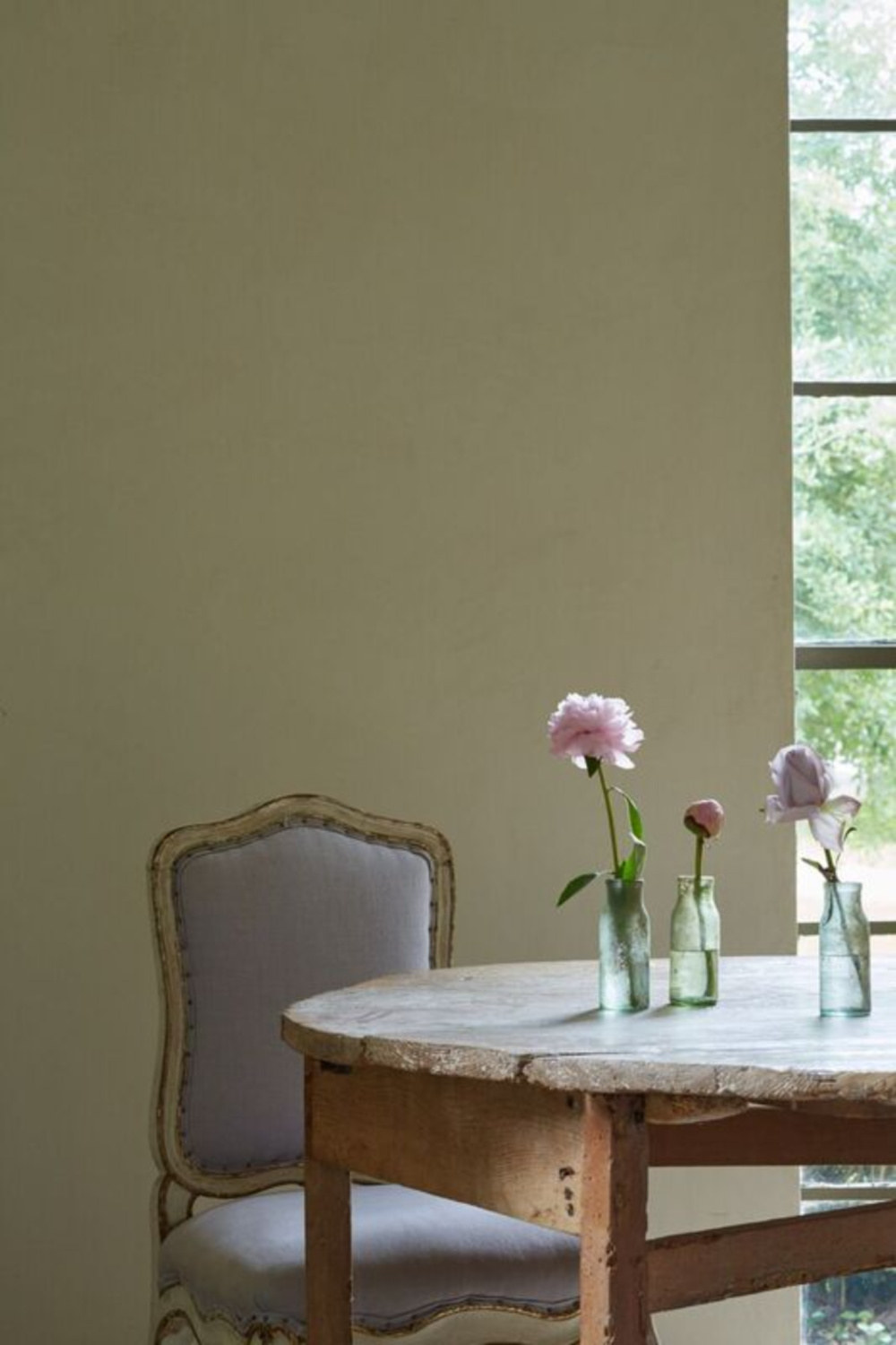 Serene, understated French country dining chair and rustic farm table with simple glass bottles used as vases - Chateau Domingue.