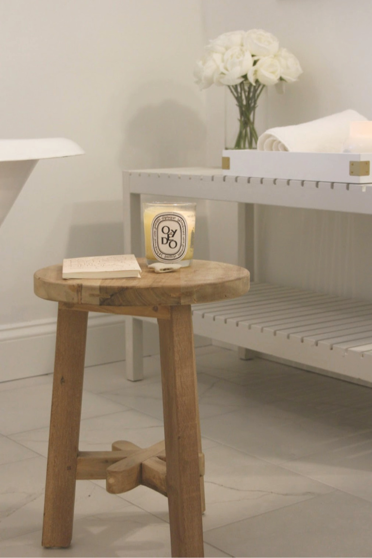 Rustic teak stool next to clawfoot tub with Diptyque candle in our master bath with calacatta like porcelain tile. #hellolovelystudio #modernfarmhouse #bathroomdecor