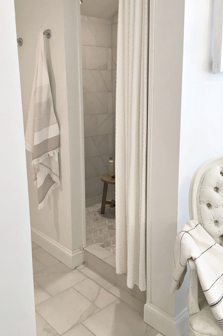 White French country bathroom with calacatta-look porcelain tile on shower walls and marble mosaic on floor. #hellolovelystudio #bathroomdesign #showertile #frenchcountry #whitebathrooms #herrinbone #marblemosaic