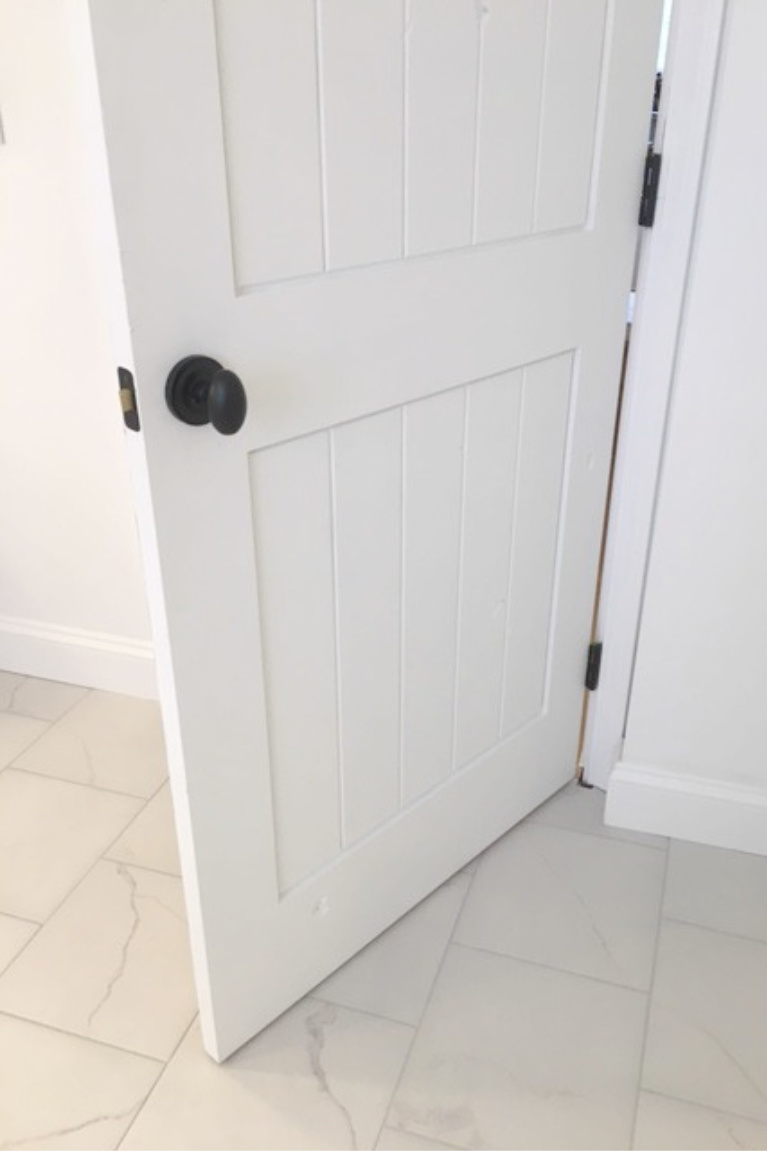 White painted alder door in our bathroom - hardware is Helmsley egg knob. Tile is calacatta-look porcelain tile. #bathroomdecor #hellolovelystudio #whitedoors