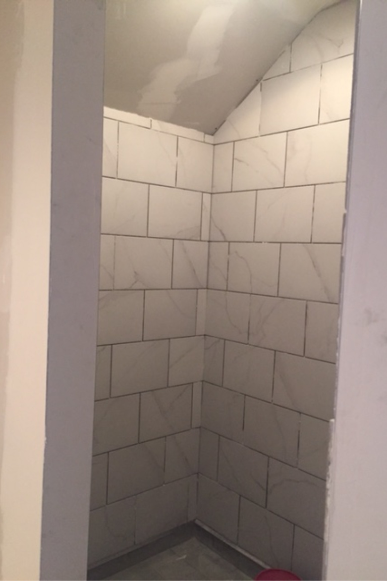 Calacatta look porcelain tile on walls of shower during renovation before grout. #hellolovelystudio #bathroomrenovation #showertile #calacattaporcelaintile