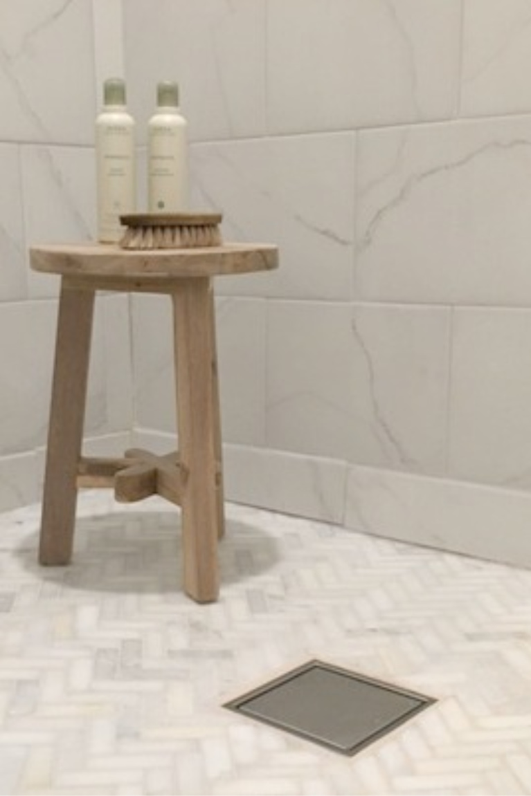 Porcelain wall tile in shower looks like Calacatta marble - floor tile is herringbone pattern honed marble mosaic tile. #hellolovelystudio #showertile #showerfloor #floortile #marblemosaic #calacattaporcelaintile #bathroomdesign