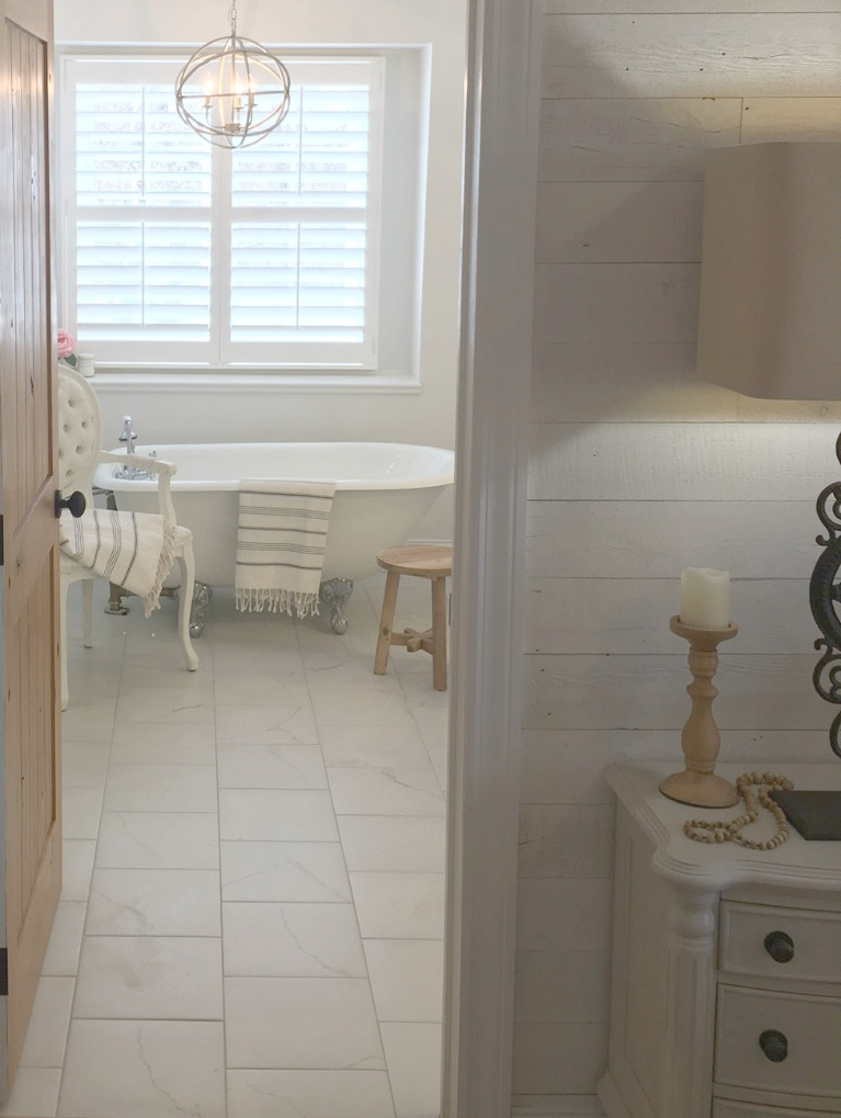 White French country master bathroom with rustic alder door,  calacatta-look porcelain tile and clawfoot tub. #hellolovelystudio #bathroomdesign #bathroomdecor #frenchcountry #clawfoottub #alderdoor