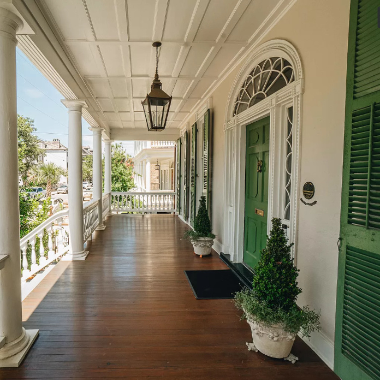 Classic and timeless piazza on Battery Street in Charleston with green shutters and beautifully stained wood floor. Peek at Charming Porch Inspiration & Decor Ideas for your home! #piazza #charlestonhouse #frontporch #greenshutters #historichome #houseexterior #southernhomes