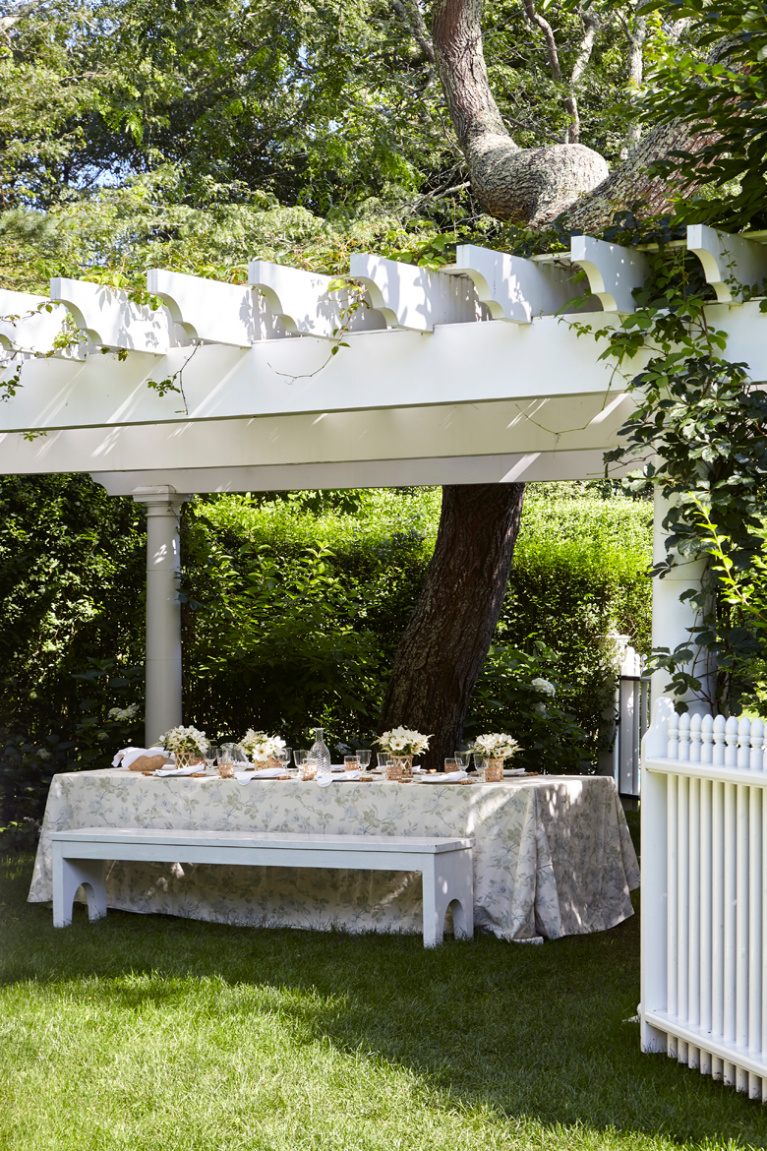 White pergola over a skirted picnic table set for lunch in the East Hampton garden of Aerin Lauder. Photo by Tria Giovan for Summer to Summer (Rudick). #aerinlauder #hamptonshome #summerhome #pergolas #tablescape #outdoordining #coastalstyle