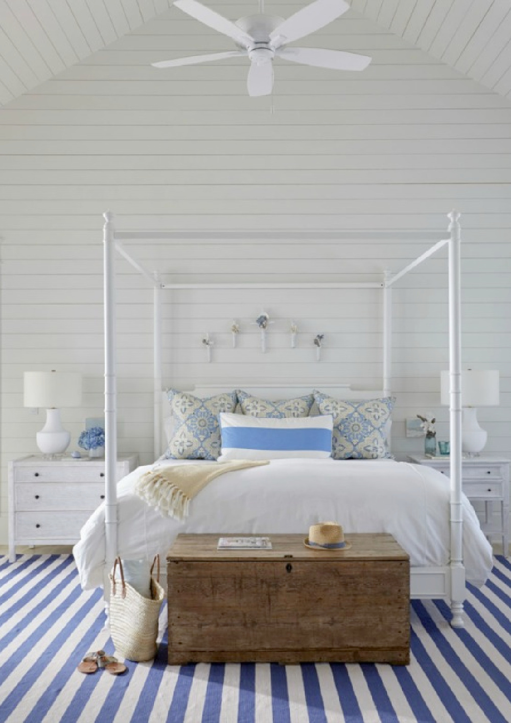 White coastal style bedroom with blue stripe rug, poster bed, and shiplap walls - architecture by Geoff Chick.