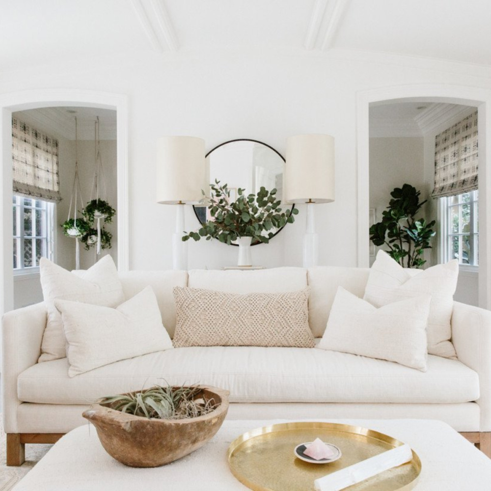 Erin Fetherston's white living room with linen sofa, rustic doubgh bowl as planter, and round brass tray. #modernfarmhouse #livingrooms #whitedecor #interiordesign