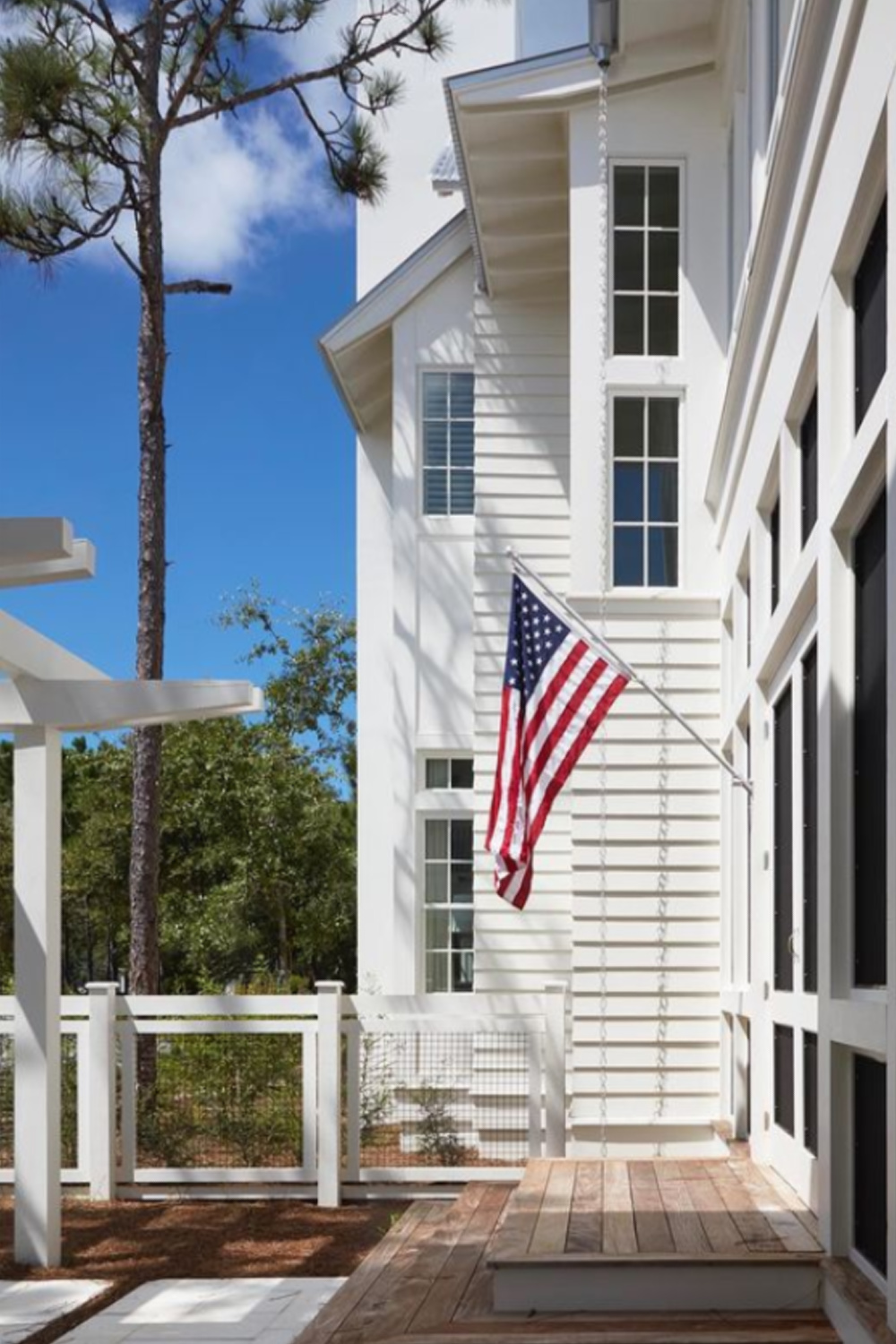Beautiful white coastal home exterior with American flag - Architect: @geoffchickandassociates Builder: Chris Clark Construction Landscape: @hortonlandworks Photo: @colleenduffleyproductions