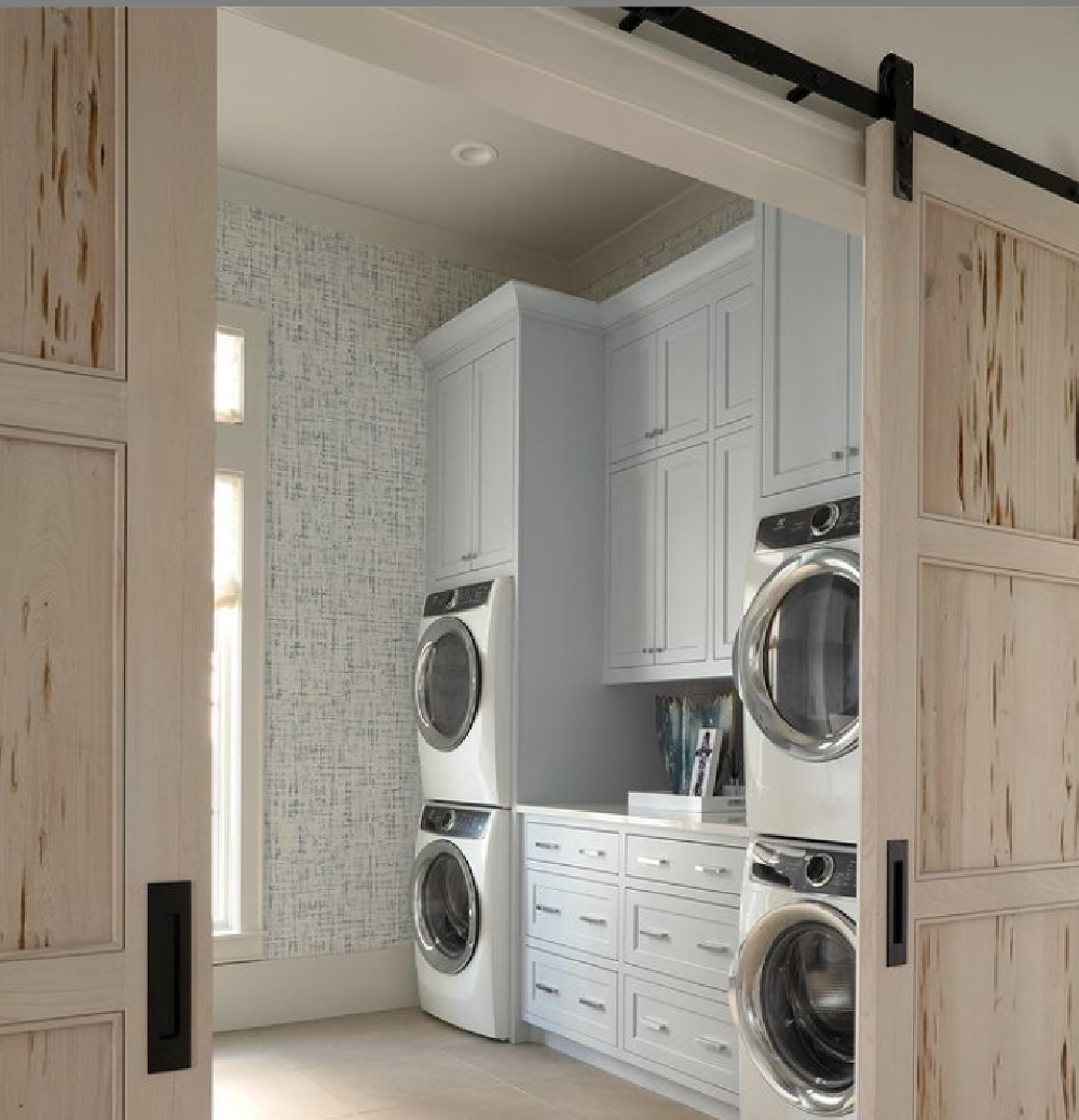 Pickled pecky cypress barn doors grace a laundry room with coastal style and light blue cabinets - architecture: Geoff Chick. #laundryrooms